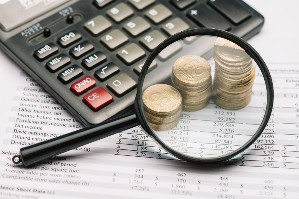 Magnifying Glass Over the Coin Stack and Calculator on Financial Report